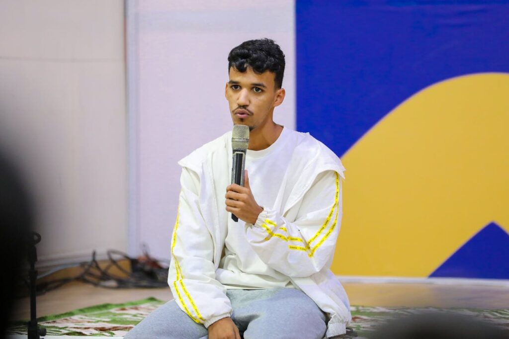 Young adult male speaking with microphone at indoor event.