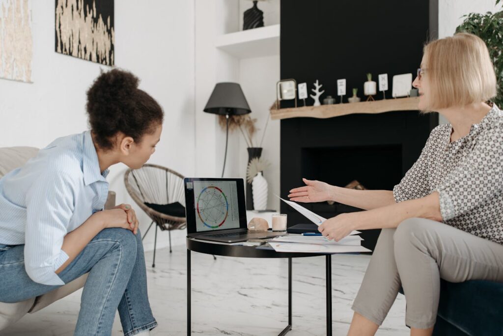 Astrologer and young woman discussing a natal chart on a laptop indoors.